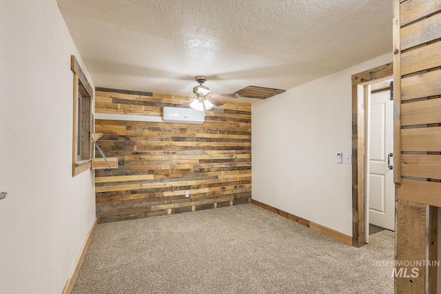 carpeted spare room featuring wooden walls, an accent wall, baseboards, ceiling fan, and a textured ceiling