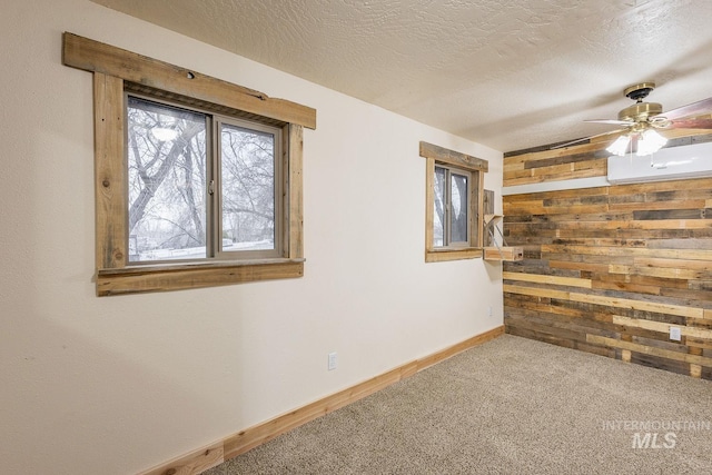 carpeted spare room with wood walls, a textured ceiling, an AC wall unit, and a ceiling fan