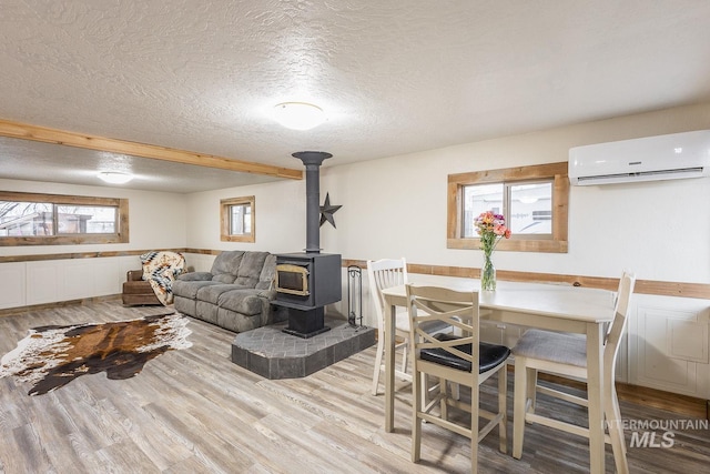 dining space featuring light wood-style flooring, a textured ceiling, an AC wall unit, and a wood stove