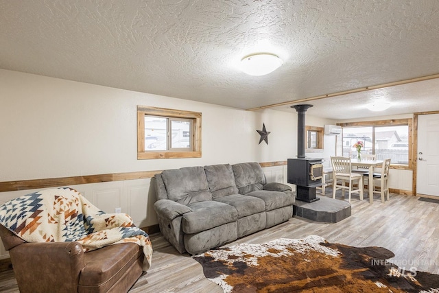 living area featuring light wood-type flooring, a wainscoted wall, a wall mounted AC, a textured ceiling, and a wood stove