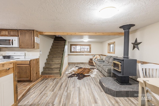 living area featuring stairway, a wood stove, light wood-style flooring, wainscoting, and a textured ceiling