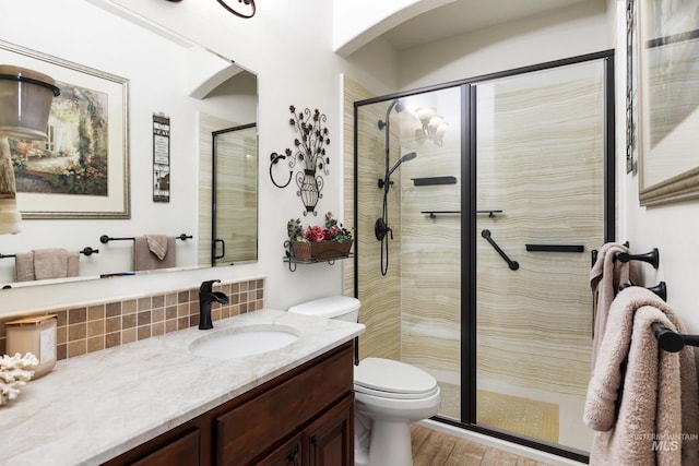 bathroom with toilet, wood finished floors, vanity, a shower stall, and tasteful backsplash