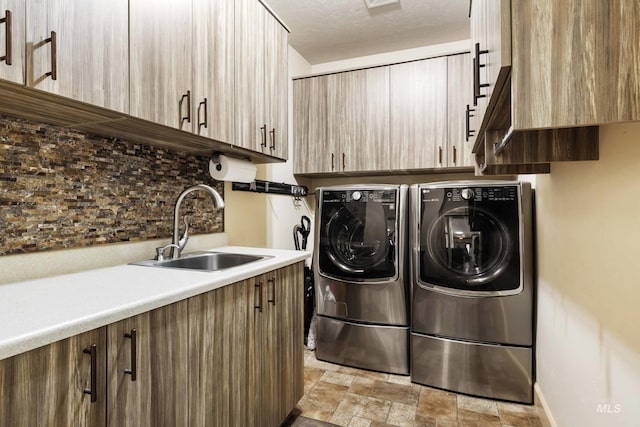 washroom featuring cabinet space, stone finish floor, a textured ceiling, washing machine and dryer, and a sink