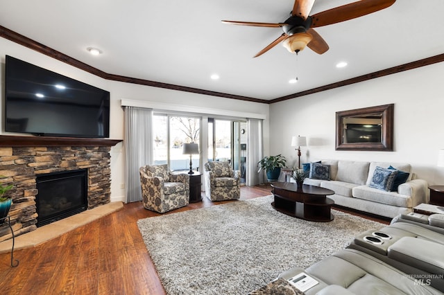 living room featuring a ceiling fan, ornamental molding, wood finished floors, and a stone fireplace