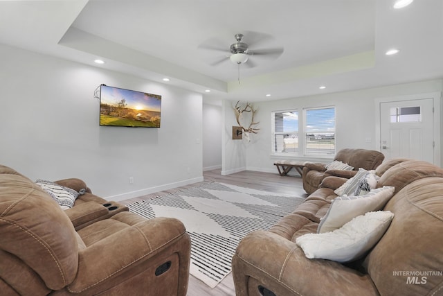 living room featuring a tray ceiling, ceiling fan, recessed lighting, baseboards, and light wood-style floors
