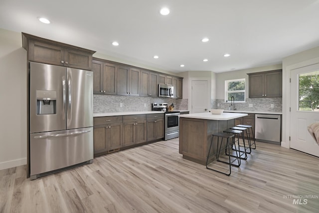 kitchen featuring appliances with stainless steel finishes, light wood-type flooring, decorative backsplash, a kitchen island, and dark brown cabinets