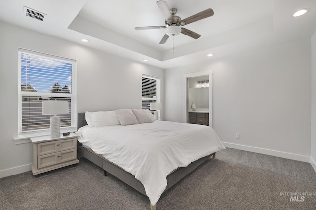 bedroom featuring recessed lighting, baseboards, a raised ceiling, dark carpet, and ensuite bathroom