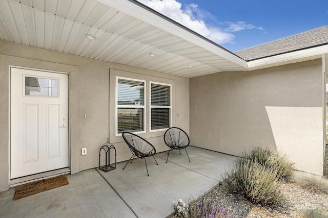 property entrance featuring stucco siding, a patio, and roof with shingles