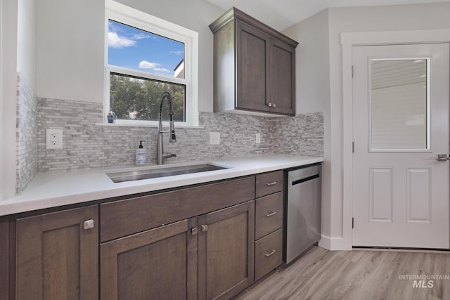 kitchen featuring stainless steel dishwasher, a sink, light wood-style floors, tasteful backsplash, and light countertops