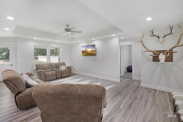 living area featuring a tray ceiling, recessed lighting, ceiling fan, light wood-style floors, and baseboards