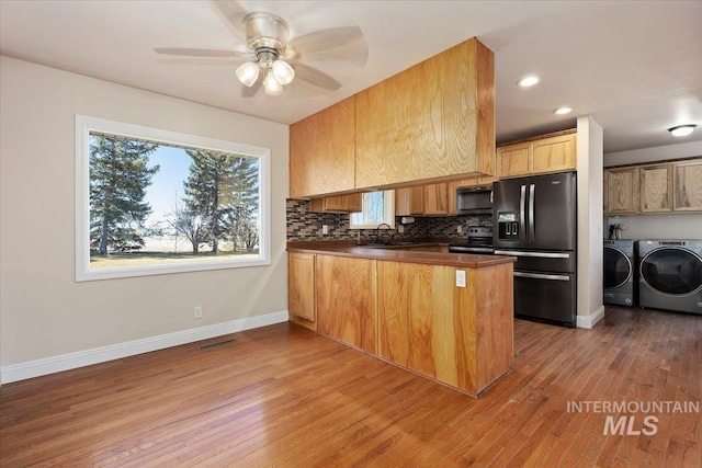 kitchen featuring electric stove, black fridge with ice dispenser, dark countertops, a peninsula, and washer and dryer