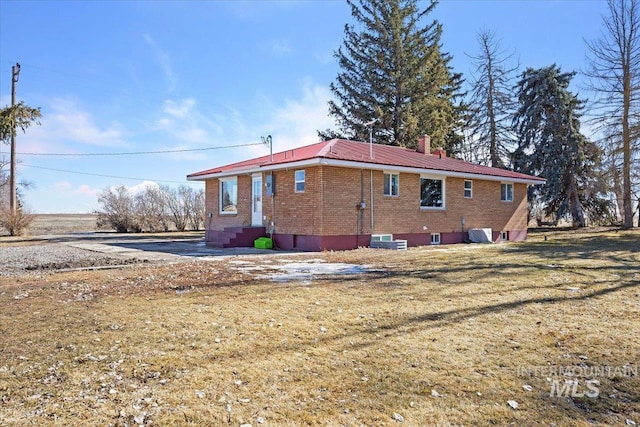 rear view of house featuring brick siding, a chimney, a lawn, entry steps, and metal roof