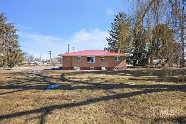 rear view of house with metal roof, a yard, and a chimney