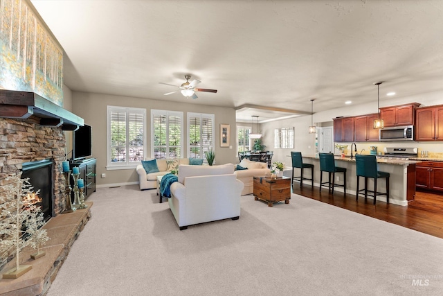 carpeted living room with ceiling fan, plenty of natural light, a sink, a stone fireplace, and recessed lighting