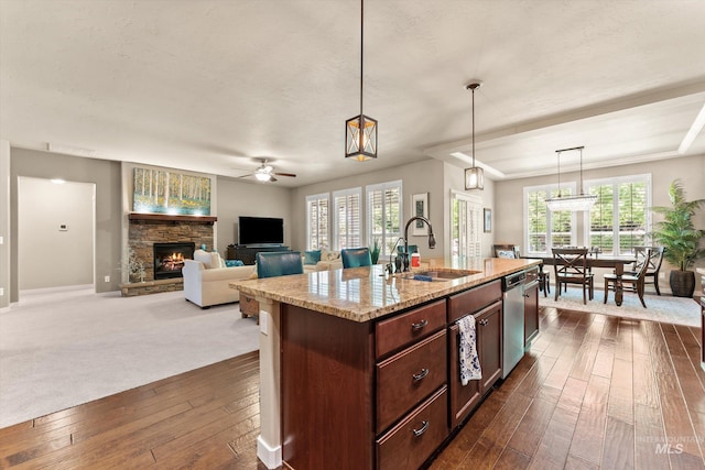 kitchen with a sink, ceiling fan, a fireplace, dark wood finished floors, and light stone countertops