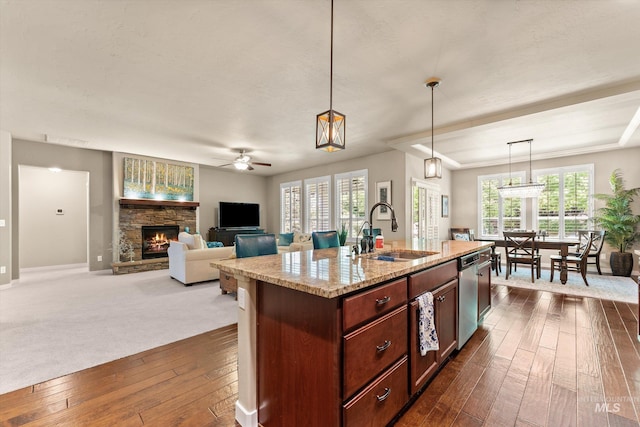 kitchen with a sink, a stone fireplace, a ceiling fan, dark wood finished floors, and dishwasher