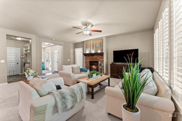 carpeted living area with ceiling fan, a stone fireplace, and baseboards