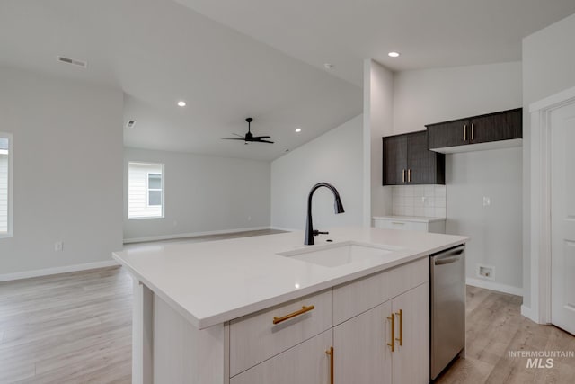 kitchen with light countertops, an island with sink, a sink, dishwasher, and light wood-style floors