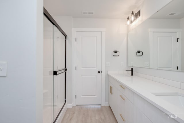 full bath featuring a sink, a stall shower, visible vents, and wood finished floors