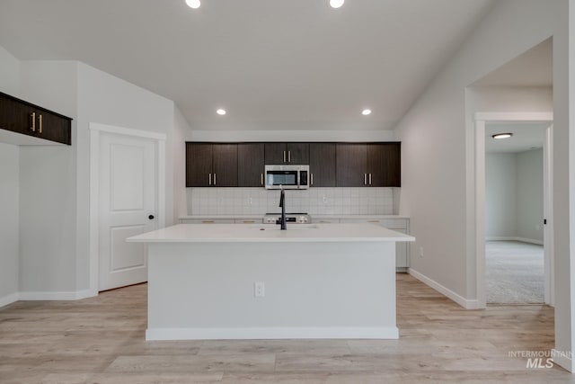 kitchen featuring dark brown cabinets, stainless steel microwave, decorative backsplash, light countertops, and a kitchen island with sink
