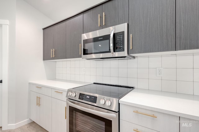 kitchen with gray cabinetry, backsplash, light countertops, and appliances with stainless steel finishes