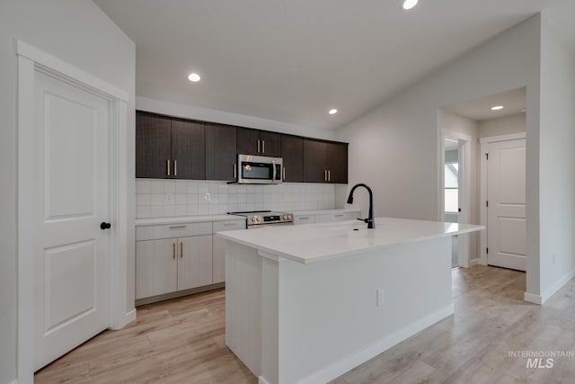 kitchen with a sink, a center island with sink, decorative backsplash, light countertops, and appliances with stainless steel finishes