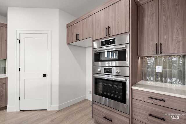 kitchen with light countertops, baseboards, double oven, and light wood-type flooring