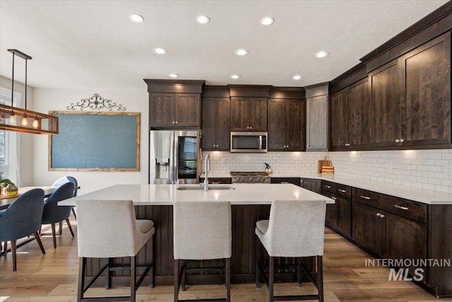 kitchen featuring wood finished floors, dark brown cabinets, light countertops, a sink, and appliances with stainless steel finishes