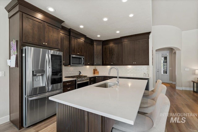 kitchen featuring dark brown cabinetry, appliances with stainless steel finishes, arched walkways, a sink, and baseboards