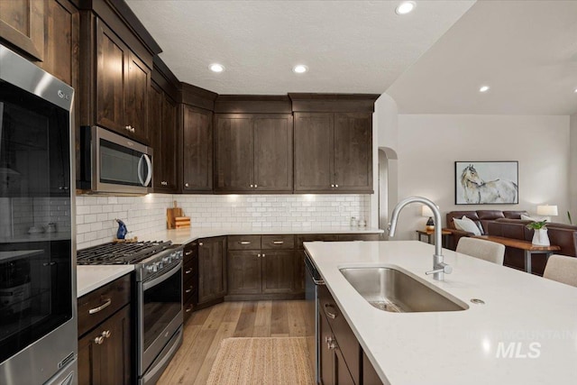 kitchen with appliances with stainless steel finishes, a sink, light countertops, light wood-style flooring, and open floor plan