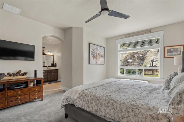 bedroom featuring light carpet, ensuite bath, arched walkways, a ceiling fan, and visible vents