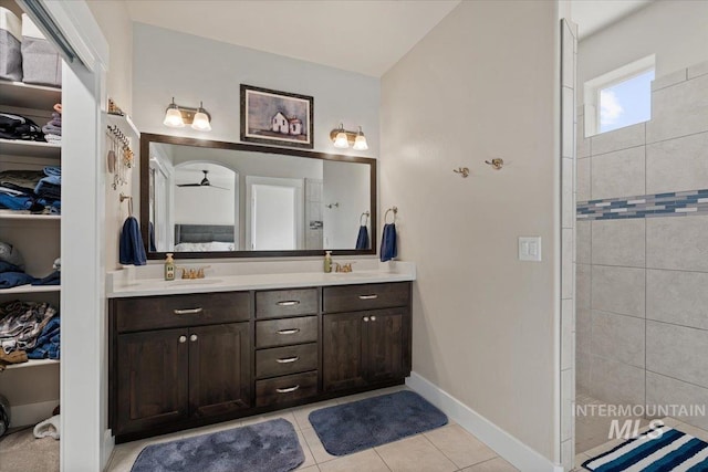 bathroom featuring tile patterned flooring, double vanity, a spacious closet, a sink, and a tile shower