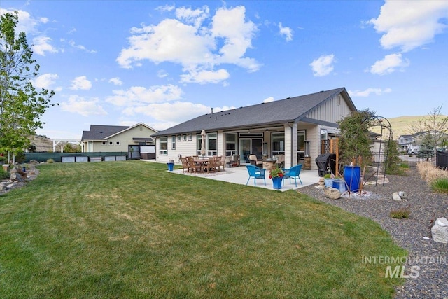 rear view of house featuring a lawn, board and batten siding, a patio area, and fence