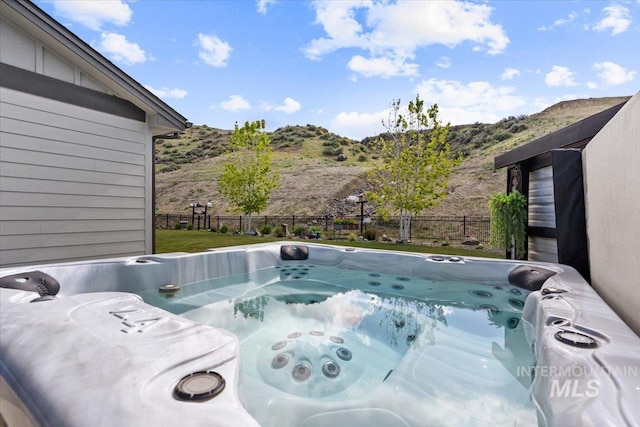view of pool with fence, a mountain view, and a hot tub