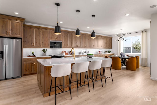 kitchen featuring black stove, sink, stainless steel fridge with ice dispenser, decorative light fixtures, and a kitchen island with sink