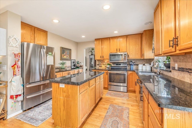 kitchen with tasteful backsplash, a center island, light wood-type flooring, stainless steel appliances, and a sink