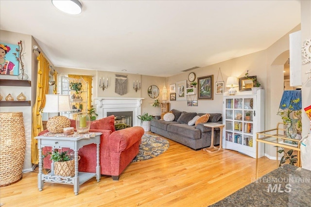 living room with arched walkways, a glass covered fireplace, visible vents, and wood finished floors