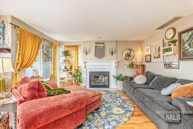 living area with visible vents, a fireplace with flush hearth, and wood finished floors