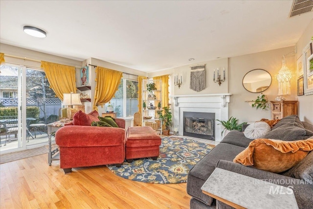 living area with a fireplace with flush hearth, wood finished floors, and visible vents