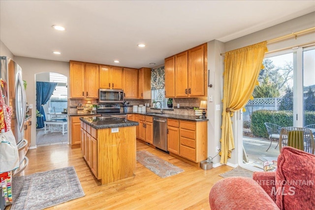 kitchen featuring light wood-type flooring, a sink, a kitchen island, backsplash, and appliances with stainless steel finishes