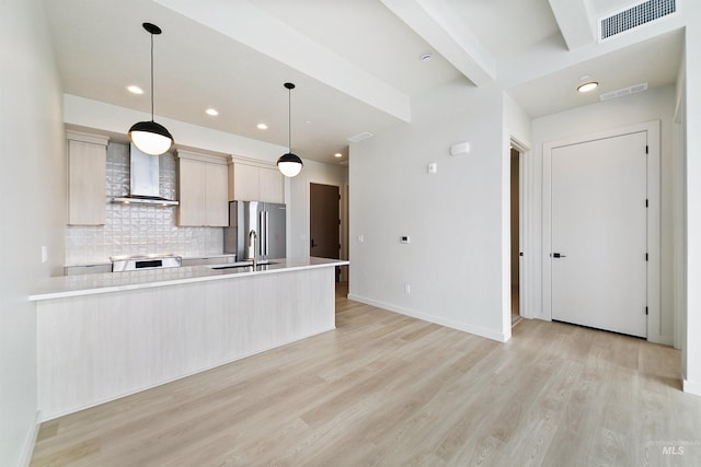 kitchen featuring light countertops, wall chimney exhaust hood, freestanding refrigerator, and a sink