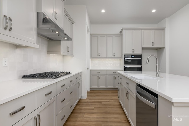 kitchen featuring appliances with stainless steel finishes, sink, light wood-type flooring, and decorative backsplash