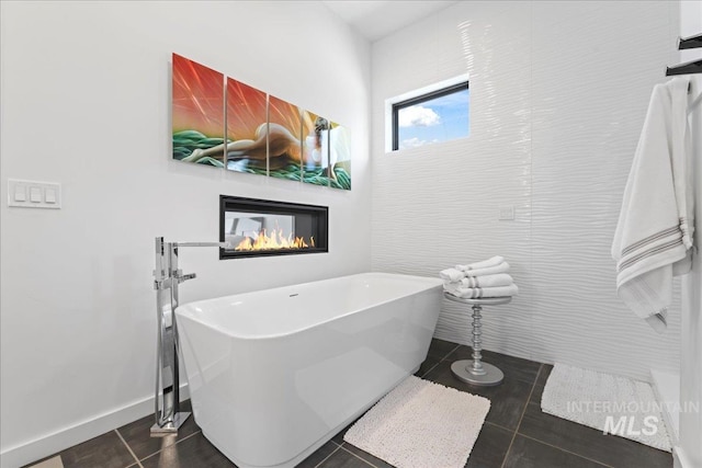3492 E Heartleaf Dr, Boise, ID 83716 - bathroom with tile patterned flooring, baseboards, a glass covered fireplace, a soaking tub, and tile walls