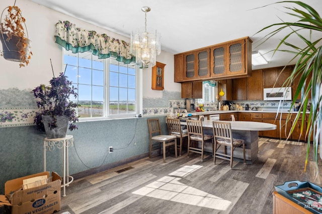 kitchen with kitchen peninsula, wood-type flooring, decorative light fixtures, backsplash, and a notable chandelier