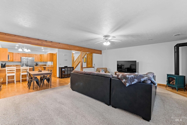 living room featuring ceiling fan, light hardwood / wood-style floors, a wood stove, and a textured ceiling