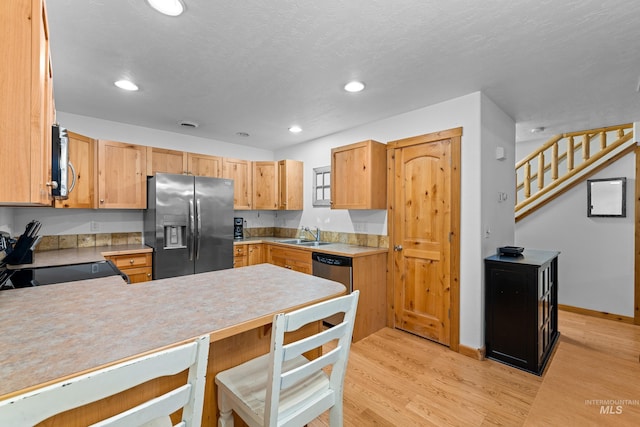 kitchen with stainless steel appliances, kitchen peninsula, light hardwood / wood-style floors, a textured ceiling, and light brown cabinetry