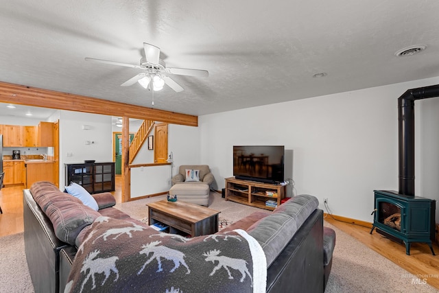 living room with a textured ceiling, ceiling fan, sink, light hardwood / wood-style flooring, and a wood stove