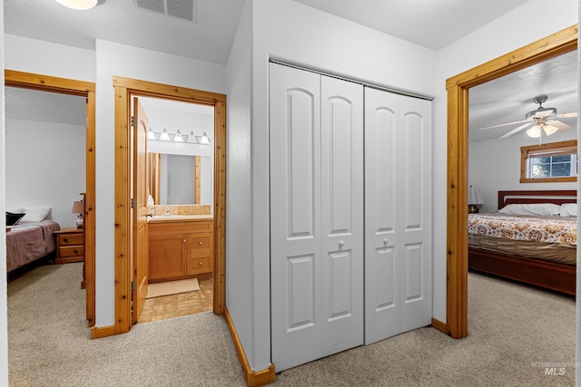 carpeted bedroom with a closet, connected bathroom, ceiling fan, and sink