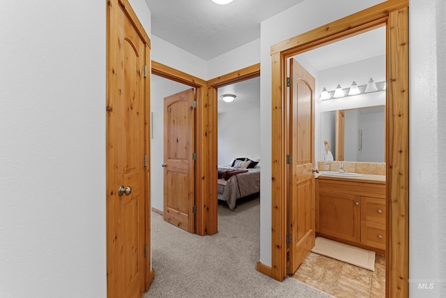 corridor with a textured ceiling, light colored carpet, and sink