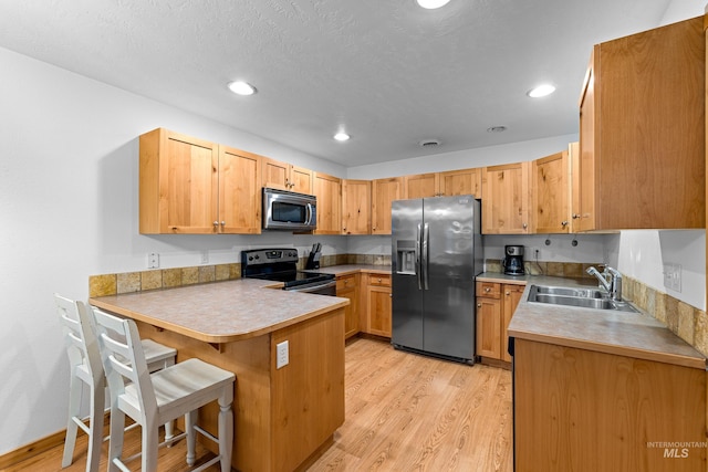 kitchen with kitchen peninsula, appliances with stainless steel finishes, a breakfast bar, sink, and light hardwood / wood-style flooring